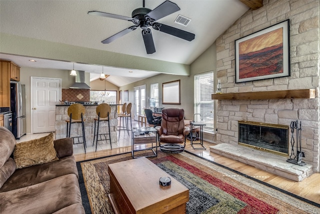 living room with a fireplace, a textured ceiling, light wood-type flooring, ceiling fan, and lofted ceiling with beams