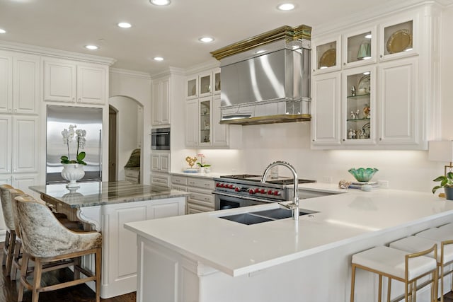 kitchen with high end appliances, extractor fan, white cabinets, and a kitchen bar