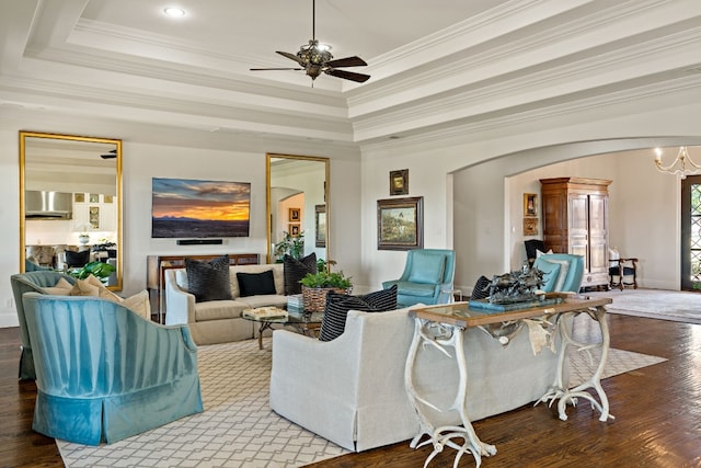 living room featuring a raised ceiling, ornamental molding, hardwood / wood-style flooring, and ceiling fan with notable chandelier