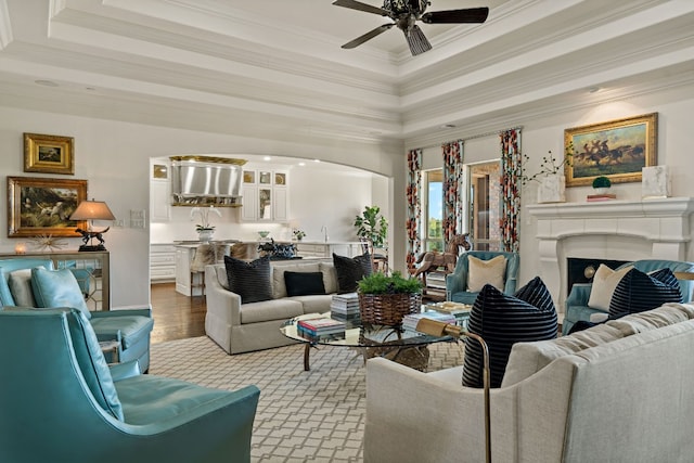 living room with ceiling fan, ornamental molding, a raised ceiling, and light hardwood / wood-style floors