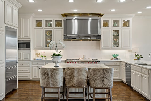 kitchen featuring appliances with stainless steel finishes, white cabinetry, a kitchen bar, ornamental molding, and wall chimney exhaust hood