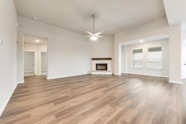 unfurnished living room featuring ceiling fan, a stone fireplace, and light hardwood / wood-style floors