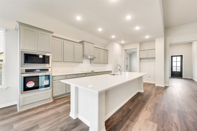 kitchen featuring built in microwave, oven, sink, and gray cabinetry