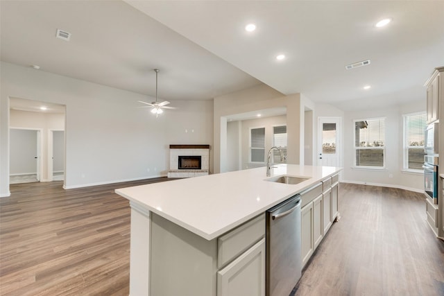 kitchen with sink, light hardwood / wood-style flooring, stainless steel dishwasher, and a center island with sink