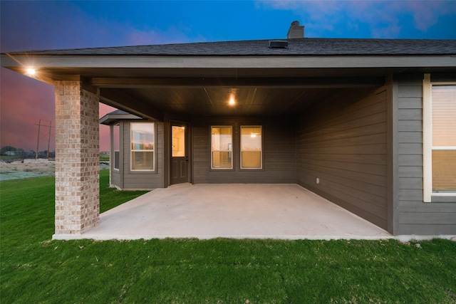 back house at dusk featuring a patio and a lawn