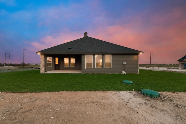 back house at dusk featuring a yard and a patio