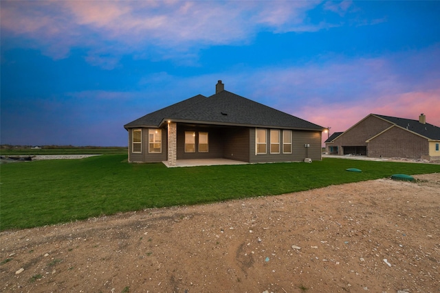 back house at dusk featuring a lawn and a patio