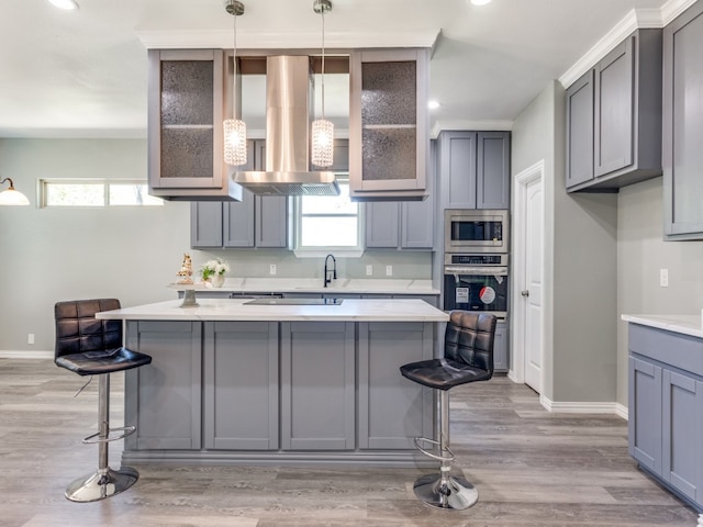 kitchen with appliances with stainless steel finishes, pendant lighting, light wood-type flooring, a kitchen breakfast bar, and range hood