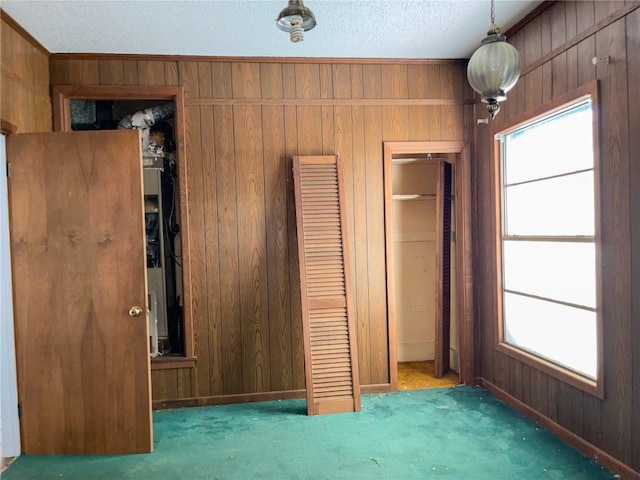 unfurnished bedroom featuring a closet, a textured ceiling, wooden walls, and dark carpet