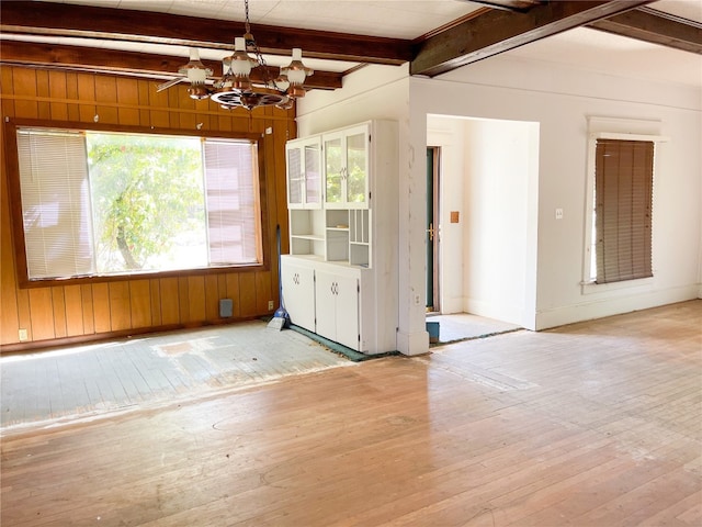 empty room with an inviting chandelier, wooden walls, light hardwood / wood-style floors, and beamed ceiling