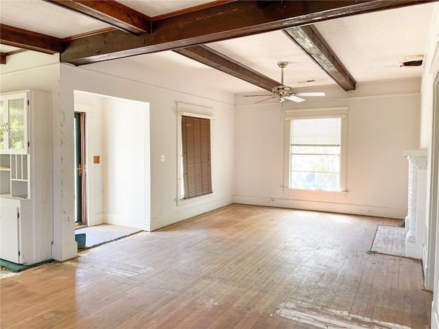 unfurnished living room with ceiling fan, light wood-type flooring, a healthy amount of sunlight, and beamed ceiling