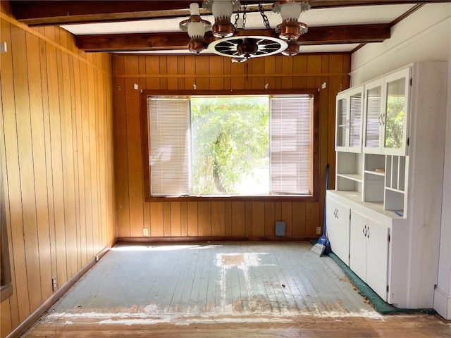 empty room featuring light hardwood / wood-style flooring, wooden walls, a chandelier, and beamed ceiling