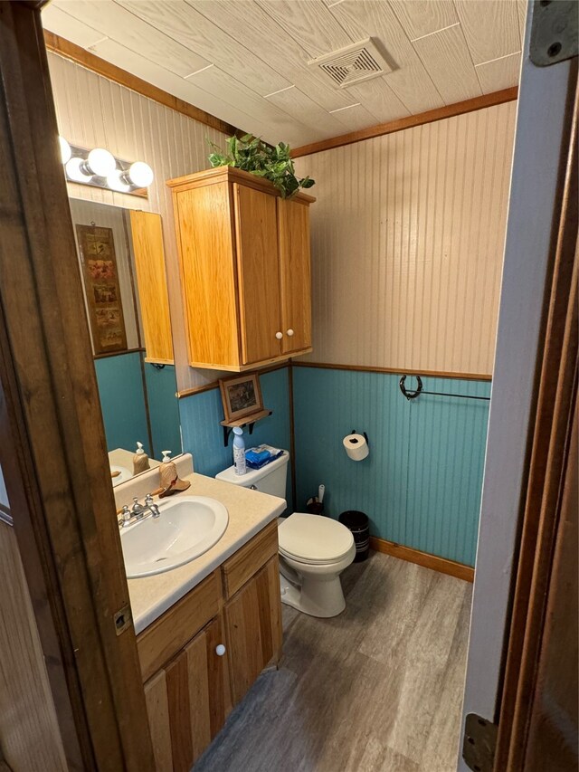 bathroom featuring hardwood / wood-style floors, toilet, vanity, wood walls, and ornamental molding