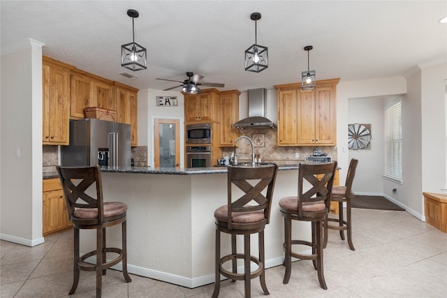 kitchen with ceiling fan, a center island with sink, wall chimney exhaust hood, appliances with stainless steel finishes, and a kitchen breakfast bar