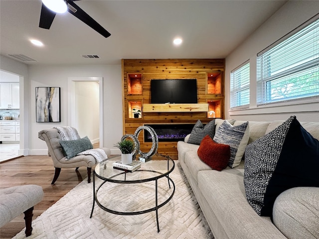 living room featuring ceiling fan, a fireplace, light wood-type flooring, and wooden walls