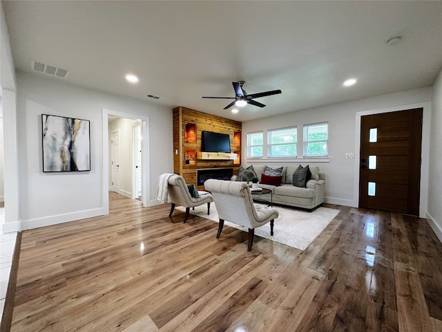 living room featuring ceiling fan, wood walls, a fireplace, and light wood-type flooring