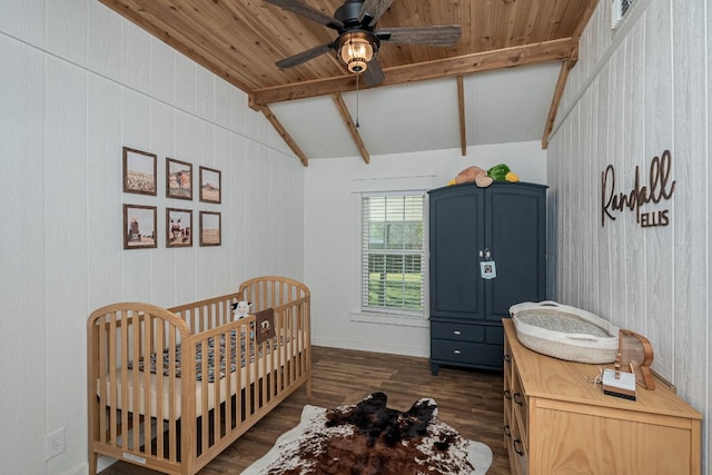 bedroom featuring a nursery area, dark wood-type flooring, ceiling fan, and vaulted ceiling with beams