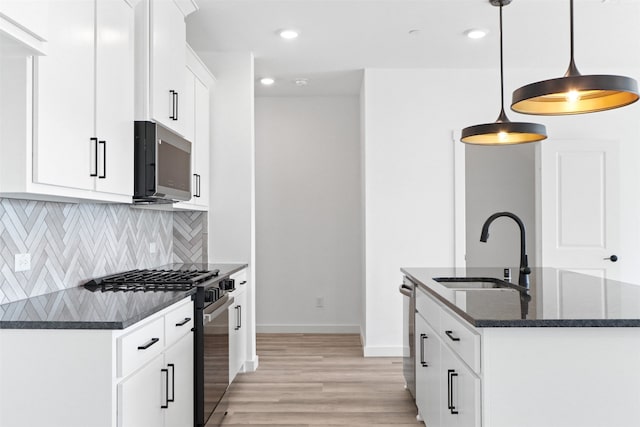 kitchen featuring pendant lighting, white cabinets, sink, stainless steel appliances, and dark stone counters