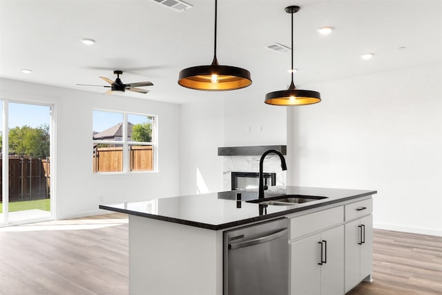 kitchen with an island with sink, sink, hanging light fixtures, white cabinetry, and dishwasher