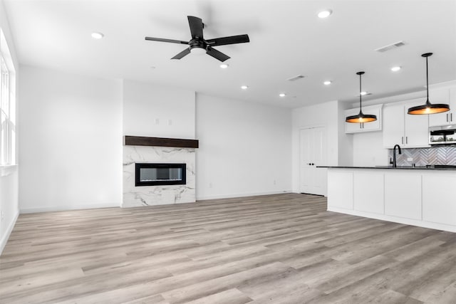 unfurnished living room with a high end fireplace, ceiling fan, sink, and light hardwood / wood-style flooring