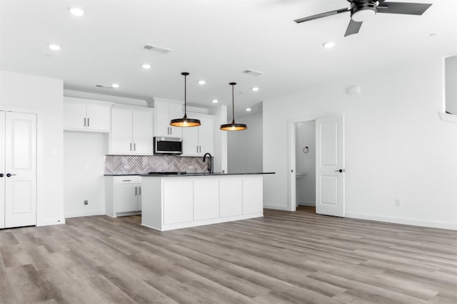 kitchen with an island with sink, pendant lighting, white cabinetry, and light hardwood / wood-style flooring