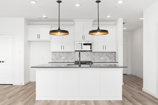 kitchen featuring a center island with sink, light wood-type flooring, dark stone countertops, and white cabinetry