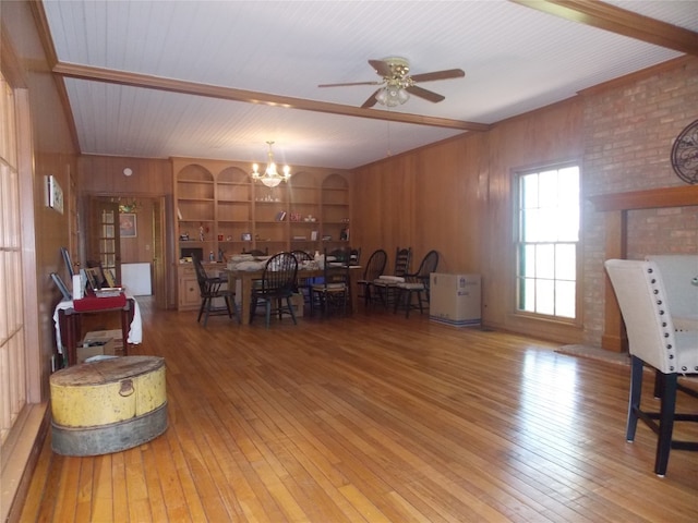 dining area featuring light hardwood / wood-style floors, ceiling fan with notable chandelier, and wood walls