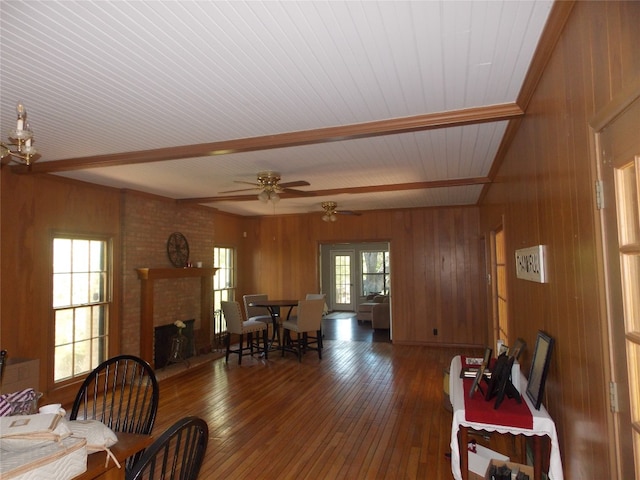 living room featuring wooden walls, ceiling fan, dark hardwood / wood-style flooring, a fireplace, and beam ceiling