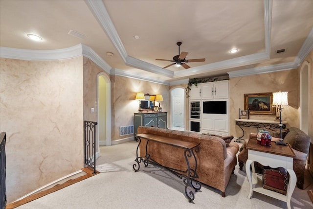 carpeted living room with a raised ceiling, crown molding, and ceiling fan