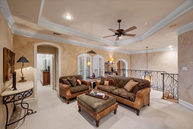 carpeted living room featuring a tray ceiling, ceiling fan with notable chandelier, and ornamental molding