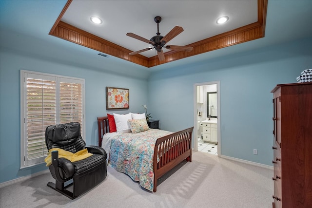 carpeted bedroom with ceiling fan, ensuite bathroom, and a raised ceiling