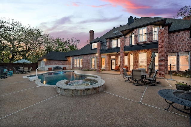 pool at dusk with an in ground hot tub and a patio