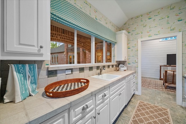 kitchen featuring dishwashing machine, sink, white cabinets, tile countertops, and vaulted ceiling