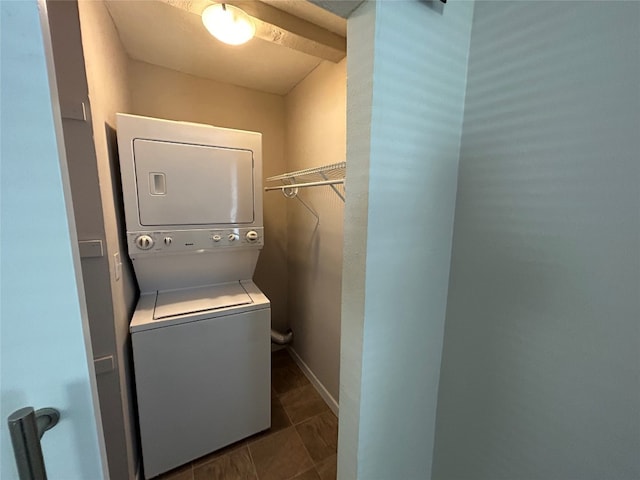 laundry room with stacked washer / drying machine and dark tile flooring