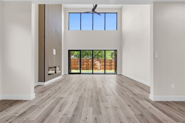 unfurnished living room with light wood-type flooring, ceiling fan, and a towering ceiling