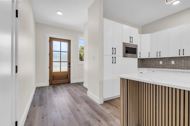 kitchen with white cabinetry, light hardwood / wood-style floors, stainless steel microwave, and tasteful backsplash