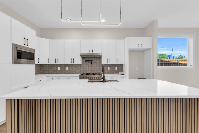 kitchen featuring stainless steel microwave, light stone counters, sink, and an island with sink