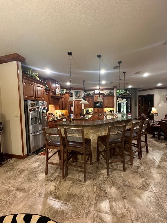 interior space with a kitchen bar, hanging light fixtures, an island with sink, and stainless steel fridge with ice dispenser