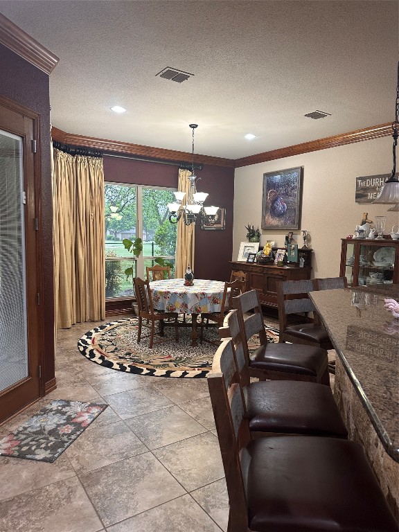 tiled dining area with a textured ceiling, ornamental molding, and a chandelier