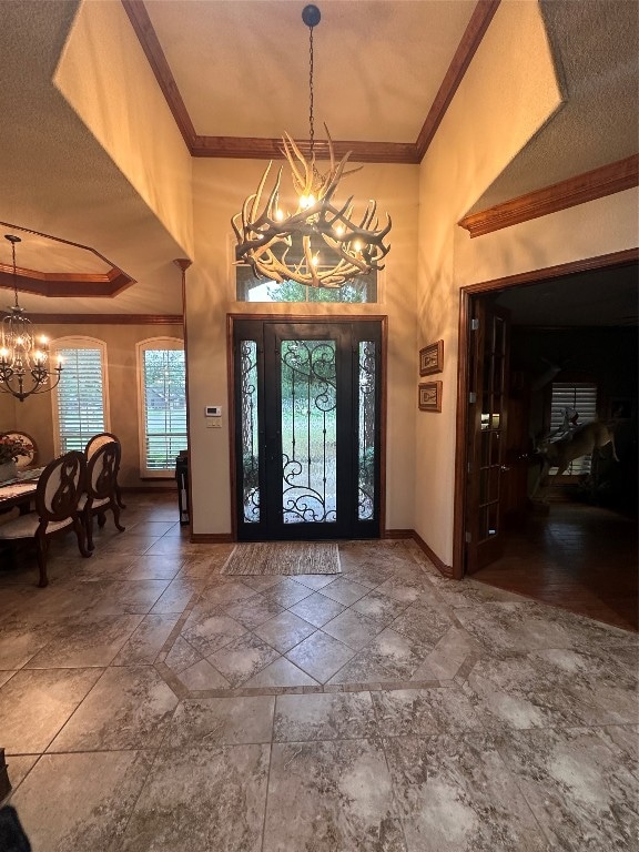 entryway featuring a notable chandelier, dark tile flooring, ornamental molding, and a textured ceiling