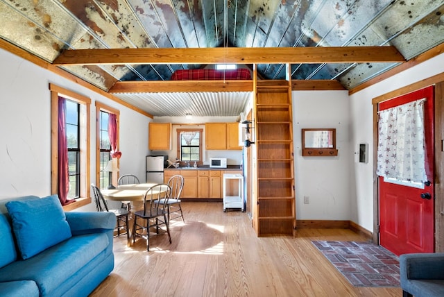 kitchen featuring crown molding, stainless steel refrigerator, beam ceiling, light wood-type flooring, and light brown cabinets