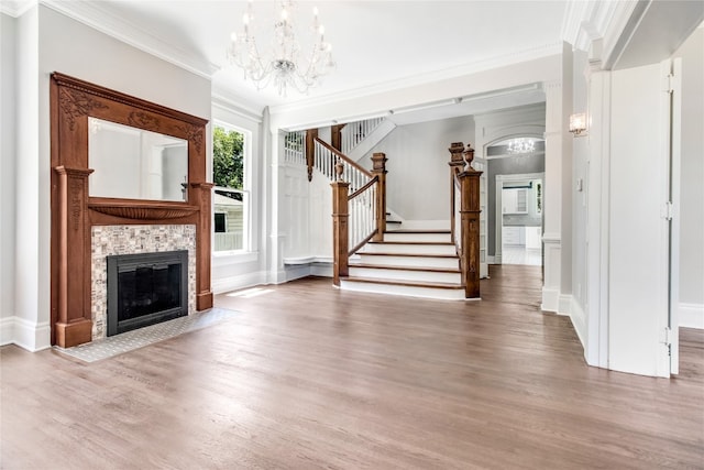 unfurnished living room featuring a tiled fireplace, crown molding, a chandelier, and wood-type flooring