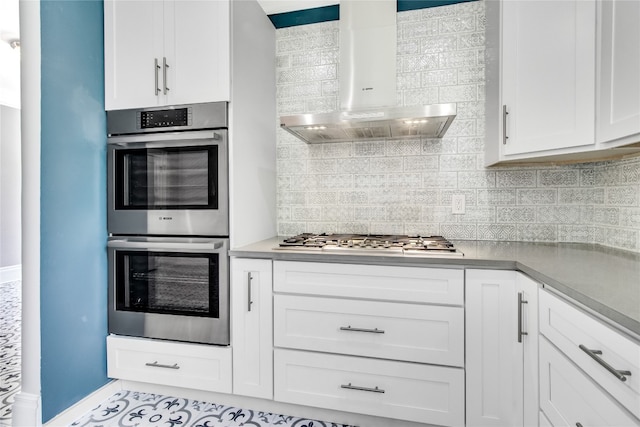 kitchen featuring white cabinets, backsplash, stainless steel appliances, and wall chimney range hood