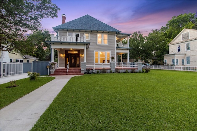 back house at dusk featuring a balcony and a lawn