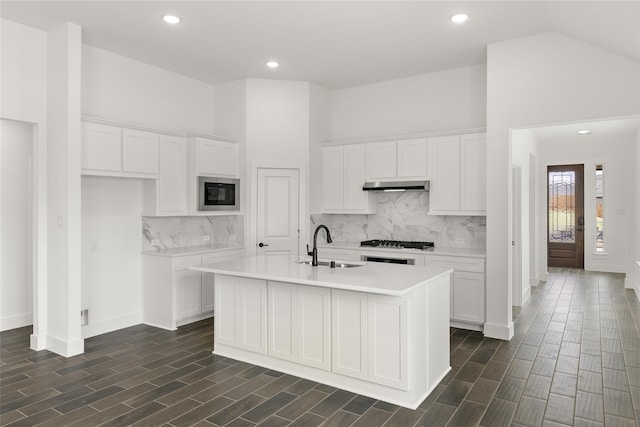 kitchen with black microwave, sink, white cabinets, stainless steel gas cooktop, and a center island with sink