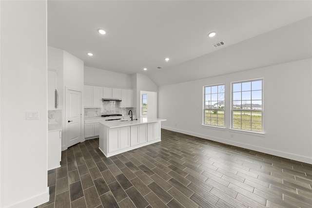 kitchen featuring sink, a kitchen island with sink, white cabinetry, decorative backsplash, and vaulted ceiling