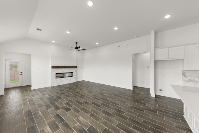 unfurnished living room featuring ceiling fan, a high end fireplace, dark hardwood / wood-style flooring, and vaulted ceiling