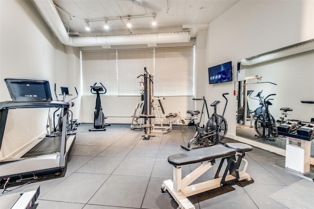 exercise room featuring rail lighting and light tile flooring