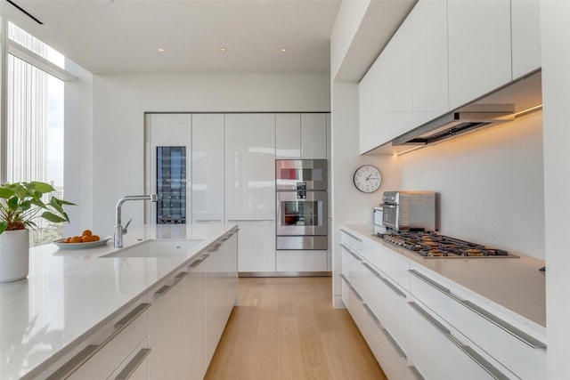 kitchen with sink, white cabinetry, light hardwood / wood-style flooring, light stone countertops, and stainless steel gas stovetop