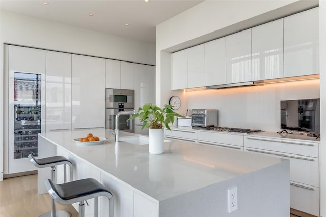 kitchen featuring a kitchen bar, light hardwood / wood-style floors, white cabinetry, a kitchen island with sink, and stainless steel gas stovetop